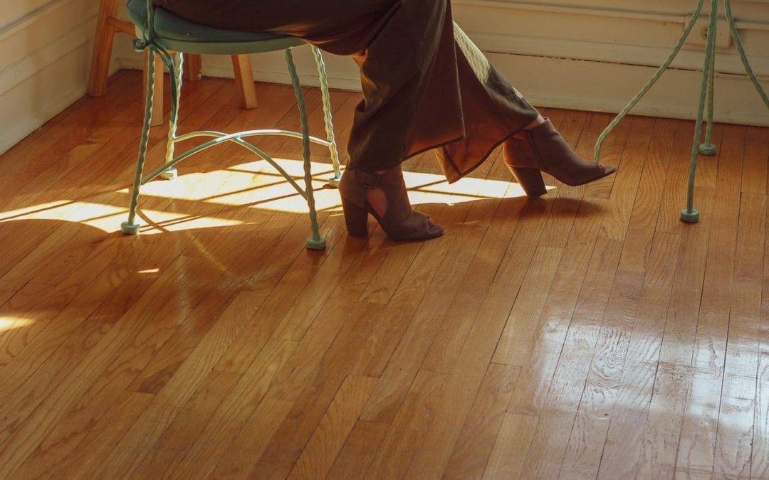 A woman wearing heels sitting in a green chair on hardwood floors